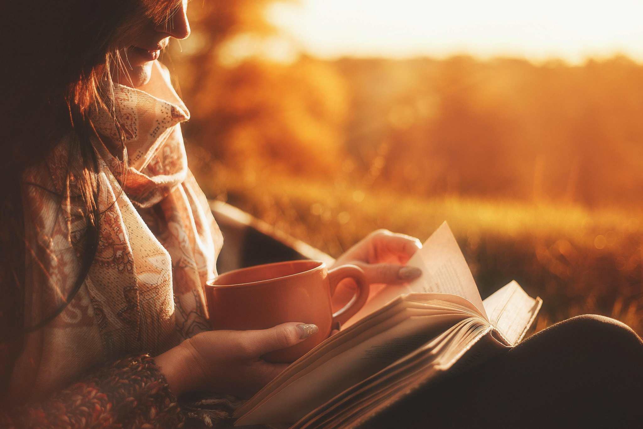 Woman enjoying a cup of Midnight Oil French Roast coffee while reading outdoors at sunset.