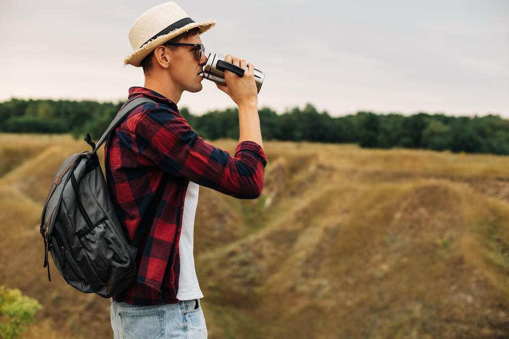 Man sipping coffee outdoors with a backpack and hat, enjoying the BOLDLY GO Medium Dark Blend.